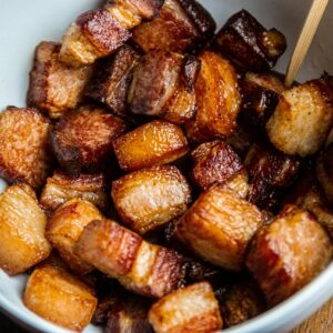 Close-up of crispy fried pork belly cubes served in a white bowl.