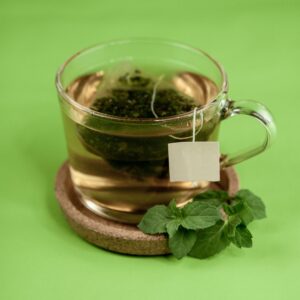 High angle of glass cup of green hot tea on ceramic cup holder with mint leaves on green surface